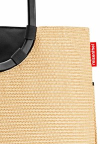 Woven straw tote bag with a black interior, rounded handles, and a red brand tag. Features a textured, natural finish.