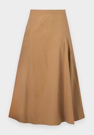 Γυναίκα με λευκή ριγωτή ζακέτα, ταιριαστό πουκάμισο με γιακά, καφέ μίντι φούστα, μπεζ κάλτσες και καφέ πλατφόρμες παπούτσια, στέκεται με τα χέρια στις τσέπες.