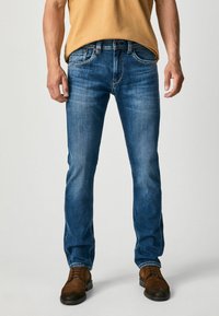 Blue denim jeans with a straight-leg fit, featuring slight fading and a five-pocket design. Paired with brown leather boots.