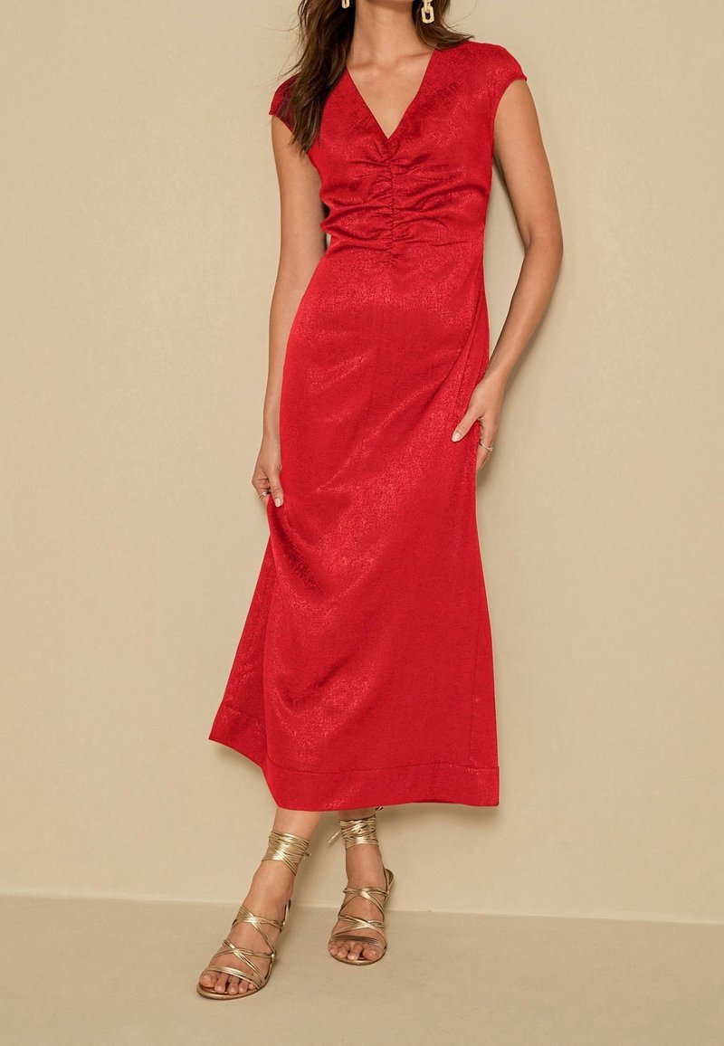 Robe rouge longueur genou avec un décolleté en V, des manches courtes, et des détails froncés au niveau du corsage. Présente une texture lisse et un léger éclat.