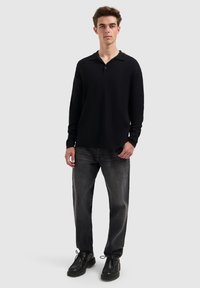 Zwarte poloshirt met lange mouwen en kraag, gecombineerd met donkergrijze recht-toe-recht-aan jeans en zwarte veterschoenen. Eenvoudig ontwerp, geen patronen.
