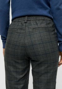 Plaid trousers featuring a grey base with black and blue lines, elastic waistband, and two back pockets. Textured fabric with a tailored fit.