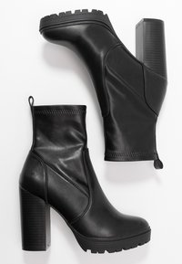 Botas de cuero negro hasta el tobillo con puntera redonda, tacón texturizado y grueso, y costuras laterales. Presentan un bucle de tirón para facilitar su uso y una suela de goma.