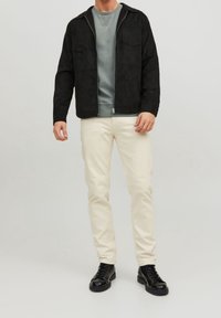 Zwarte fluwelen jas met voorzakken, grijze crewneck shirt, crèmekleurige broek en zwarte veterschoenen. Eenvoudig, functioneel ontwerp.