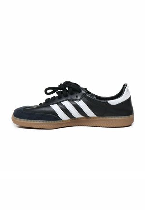 Pantofle sportive alb-negru cu un superior din suede și piele. Prezintă trei dungi albe, șireturi negre și o talpă din cauciuc de culoare caramel.