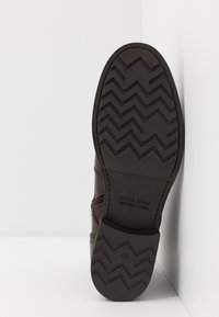 Suela de zapato de cuero marrón con un patrón de banda de rodadura en zigzag, con una marca grabada y un marcador de tamaño. El tacón tiene un acabado suave.