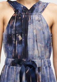 Φόρεμα χωρίς μανίκια με μπλε και μοβ αφηρημένο σχέδιο, διακοσμημένο με σούρες στο ντεκολτέ και ζώνη από το ίδιο ύφασμα δεμένη στη μέση.