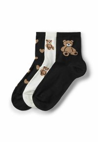 Drei Knöchelsocken in Schwarz und Weiß; die schwarzen Paare zeigen einen braunen Teddybären und Herzen, das weiße Paar hat mehrere kleine Teddybär-Motive.