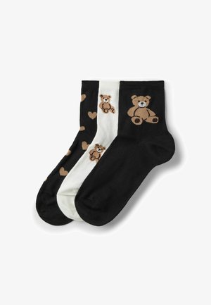 Drei Knöchelsocken in Schwarz und Weiß; die schwarzen Paare zeigen einen braunen Teddybären und Herzen, das weiße Paar hat mehrere kleine Teddybär-Motive.