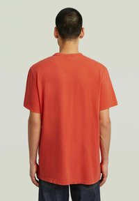 Camiseta de algodón de manga corta y cuello redondo en un brillante color rojo, con un corte relajado, dobladillo recto y sin logotipos ni gráficos visibles.