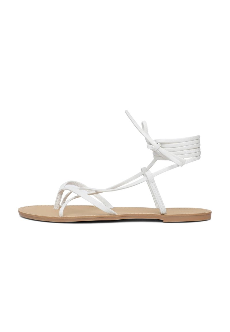 Sandali piatti bianchi presentano fasce sottili, un design minimalista e una suola piatta color beige. Le fasce sono realizzate in un materiale liscio con un dettaglio con lacci.