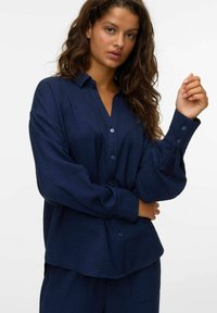 Camicia button-up blu navy con un tessuto morbido e texture, vestibilità rilassata e maniche lunghe. Presenta un colletto e polsini con bottoni.
