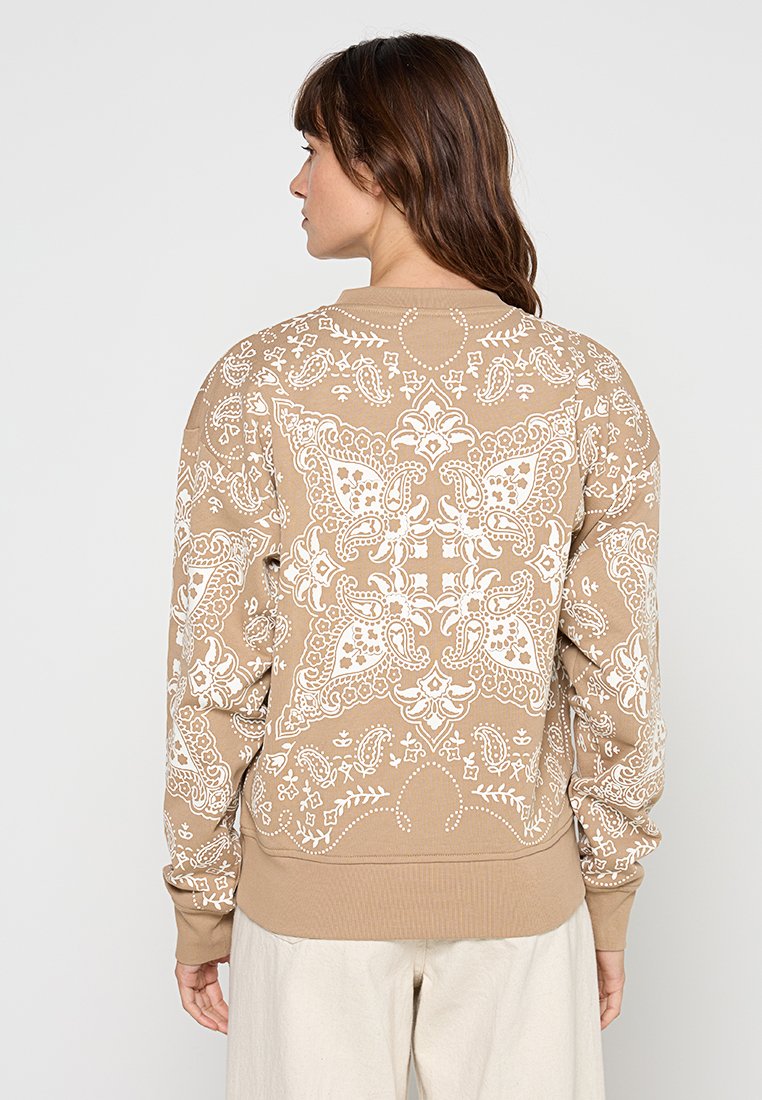 Beige sweatshirt met een groot wit paisley- en bloemenpatroon op de achterkant, geribbelde manchetten en zoom. Zachte stof met een ontspannen pasvorm.