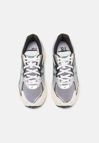 Běžecké tenisky z prodyšné síťoviny v bílo-černé barevné kombinaci, s zelenými akcenty, polstrovanou podrážkou a tradičním šněrováním.