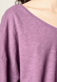 Haut en coton léger de couleur lavande, doux, avec un large décolleté en V et des manches courtes, présentant une coupe décontractée et une texture subtile.