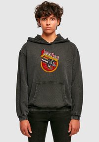 Melnas kapuces sporta krekls ar priekšējo kabatu, ribinātām piedurknēm un grafisku zīmējumu ar ģitāru un uzrakstu "Judas Priest" treknajiem burtiem.