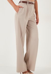 Beige, széles szárú nadrág sima anyagból, magas derékkal, elülső zsebekkel és barna bőr övvel kiegészítve.