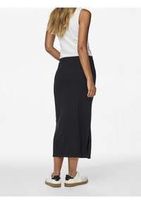 Lång, ribbad svart kjol med en sidoklyfta, kombinerad med vita sneakers med svart accent. Lätt textur, åtsittande midja.