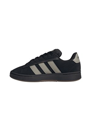 Zapatilla baja negra con rayas grises, cordones negros y una suela gruesa negra, vista lateral aislada sobre fondo blanco.