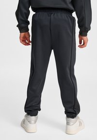 Mörkgrå sportbyxor med elastisk midja, avsmalnande muddar och kontrasterande sidostrick. Bärs med ljusa sneakers.