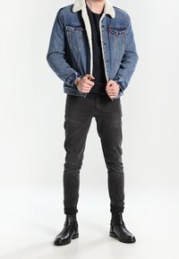 Jeansjacka med vit fleecekrage, blå färg, framfickor, kombinerad med svarta skinny jeans och svarta ankelboots.