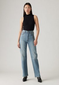 Mustast ribidest varrukateta top kõrgvöökohal heleroheliste sirgete säärega teksadega. Sile tekstuur, pehme pleekimine ja minimaalsed õmbluse detailid.