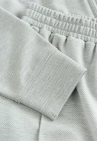 Vaaleanharmaa, teksturoitu kangas, jossa on ribbineulottu vyötärönauha ja resorimitalliset hihat. Kuvio koostuu pienistä, tasaisesti sijoitetuista pisteistä.