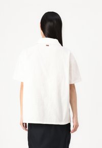 Chemise blanche à manches courtes en lin, dotée d'une coupe décontractée, d'un col et d'une petite étiquette logo dans le haut du dos.