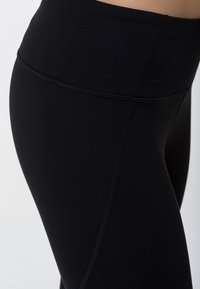 Černé legíny vyrobené z elastického materiálu, s vysokým pasem, hladkou texturou a kontrastním švem po straně.