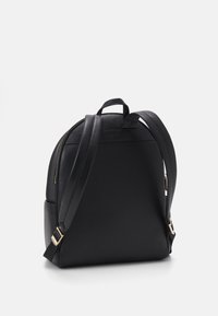 Sac à dos noir en matériau texturé avec un design arrondi. Équipé de quincaillerie dorée, de bretelles réglables et d'une poignée supérieure.