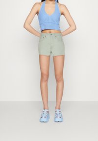 Top corto de punto azul claro con patrón texturizado, combinado con shorts de mezclilla verde claro con dobladillo deshilachado y sandalias azules de plataforma.
