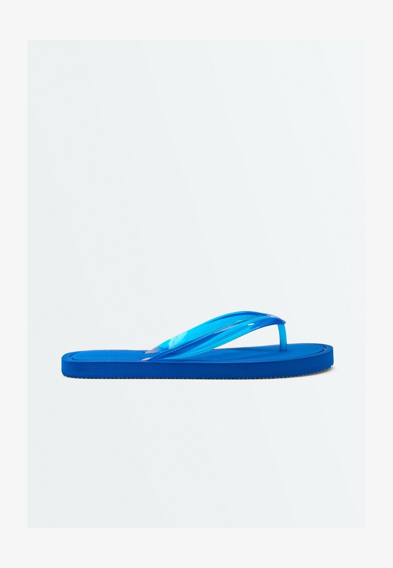 Une sandale tongs bleue avec une semelle plate et des brides bleues translucides, isolée sur un fond clair uni.