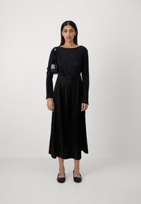 Svart langermet topp med vertikale folder, parret med en flytende svart satin midi skjørt. Tilbehør inkluderer en liten svart håndveske og flate sko.