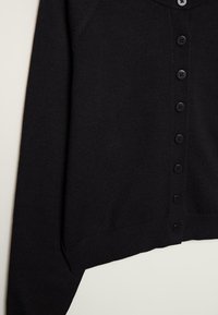 Cardigan noir en tricot avec manches longues et une rangée de boutons noirs sur le devant, présenté sur un fond neutre.