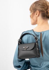 Borsa a mano in pelle nera con un accento di un'ape argentata, manico arrotondato e tracolla a catena, con dettagli borchiati lungo i lati.