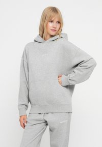 Sweatshirt cinza feito de um tecido suave, com capuz, bolso tipo canguru e punhos canelados. A parte da frente apresenta detalhes discretos do logótipo.