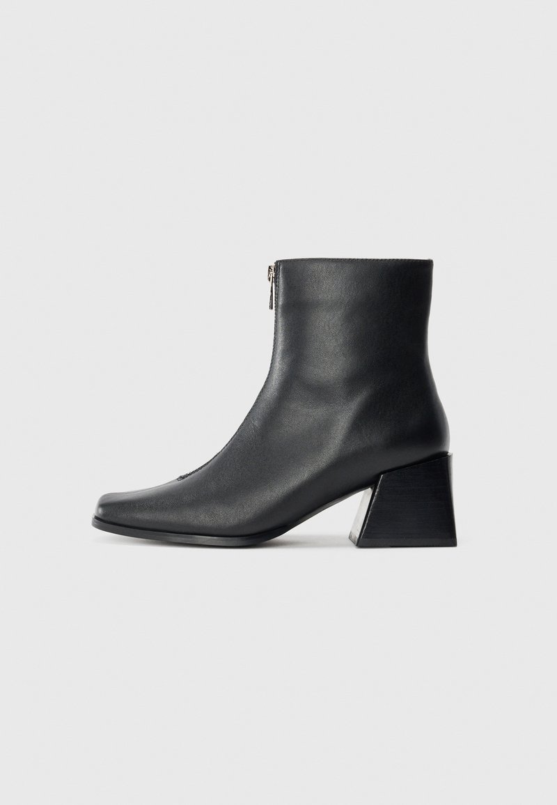 Black leather ankle boot with square toe, side zipper, and block heel against plain light background.