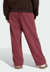 Pantalones deportivos burdeos de corte holgado, con una cintura alta y textura suave. Pliegues visibles y aberturas de pierna ligeramente ajustadas.