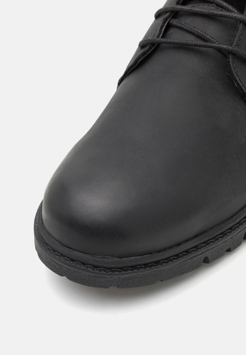 Scarpa in pelle nera con punta arrotondata e suola in gomma testurizzata. Presenta una cucitura minimale lungo il bordo e lacci neri.