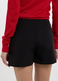 Pantaloni neri con una vestibilità su misura, realizzati in tessuto liscio, con vita media e tasche laterali discreta, abbinati a un maglione rosso con texture.