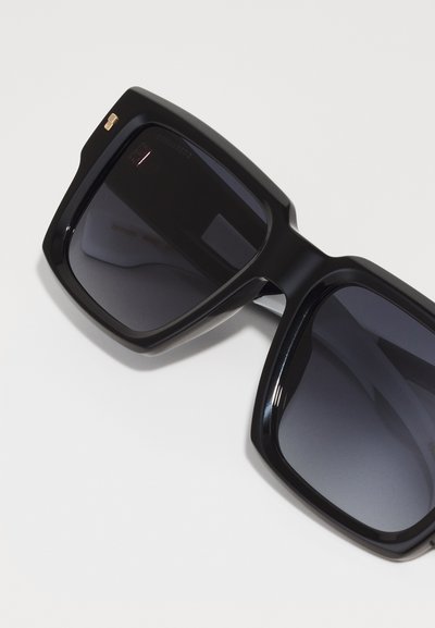 Occhiali da sole neri oversized con lenti scure, design a forma quadrata e finitura lucida. Presentano un piccolo accento dorato sul lato.