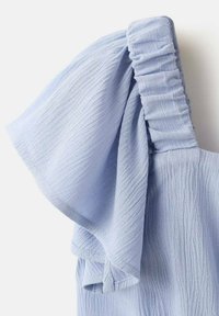 Lyseblå bluse med tekstureret stof. Har en rynket, elastisk skulder og bred, flydende ærme for en løs pasform.