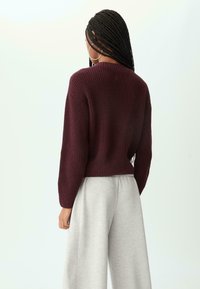 Burgunderfarbener Strickpullover mit gerippten Kanten, kombiniert mit hellgrauen Jogginghosen. Der Pullover hat eine lockere Passform und fallende Schultern.