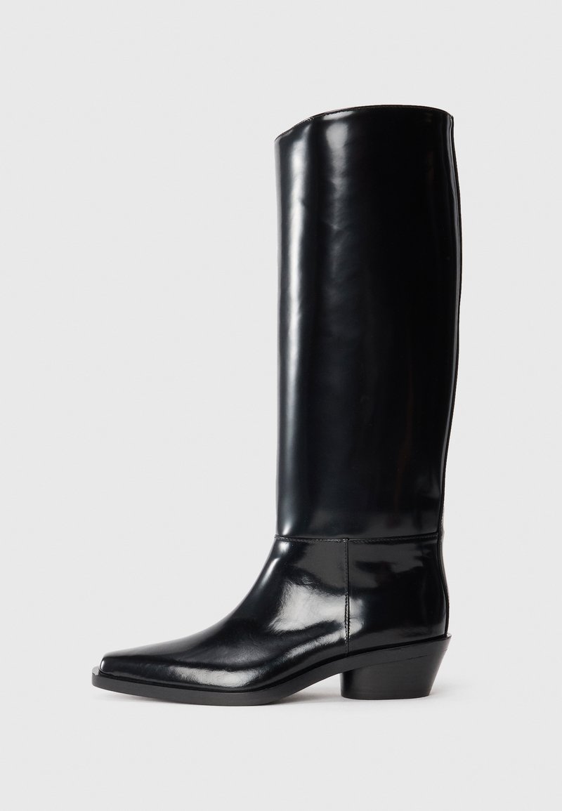 Knee-high musta läikivast nahast saapad terava ninaga ja väikese koonusakka pöidla, millel on sile tekstuur ja minimaalne õmblus.
