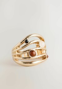 Guld-tone ring med et åbent, bølget design; har tre dekorative sten i sort, hvid og rødbrun. Glat, poleret overflade.