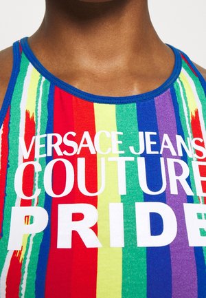 Personne portant un débardeur à rayures arc-en-ciel avec une bordure bleue et un texte blanc indiquant ""Versace Jeans Couture Pride"" sur la poitrine.