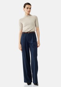 Top beige a maniche corte abbinato a pantaloni a gamba larga a righe navy e una cintura marrone. Scarpe nere lucide completano l'outfit.