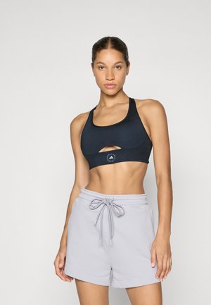 Reggiseno sportivo nero con un design a ritaglio e logo sulla fascia, abbinato a pantaloni corti grigi chiari con cordino. Texture liscia e forma aderente.