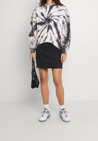 Sudadera de tie-dye en blanco y negro con mangas largas, combinada con una falda de mezclilla negra. Acentuada con un pequeño bolso negro y zapatillas blancas.