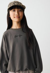 Sweatshirt gris avec un col rond et une coupe décontractée, portant le texte "Sports Crab". Associé à une casquette à imprimé léopard. Texture lisse, design décontracté.
